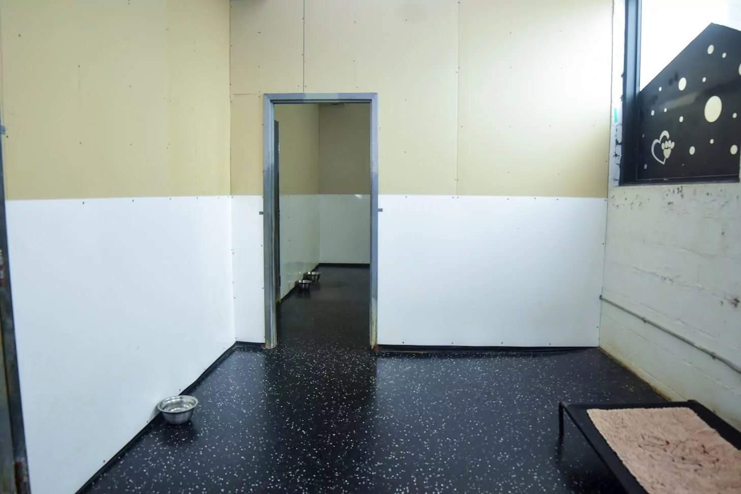 Empty kennel room with dog bed and bowls.