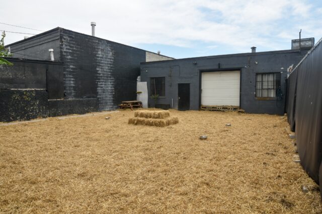 Outdoor area with hay, grey building background.